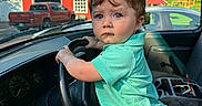 Vincent is registered to the contest to win money with this photo: child, toddler, baby, boy, portrait, car, steering_wheel, driver_seat, adult_hand, outdoor, red_barn, pickup_truck, greenery, sunlight, blue_eyes, brown_hair, turquoise_shirt, plaid_shorts, vehicle_interior, family