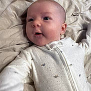 Weston is registered to the contest to win money with this photo: baby, infant, onesie, blanket, sleepwear, face, head, skin, child, newborn, lying_down, expression, cute, soft, fabric, comfort, indoors, portrait, small, adorable