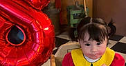 Annaya is registered to the contest to win money with this photo: toddler, child, balloon, number_8, high_chair, colorful_clothing, indoor, flooring, checkered_floor, yellow_chair, wooden_furniture, person, curly_hair, pigtails, playful, birthday, party, smile, young_child, home