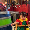 Annaya joined the competition — help win amazing prizes! toddler, child, high_chair, colorful_clothing, pigtails, indoor, barrel, wooden_furniture, checkered_floor, staircase, door, number_23, red_wall, green_clothing, yellow_collar, black_shoes, curious_expression, hand_reaching, person, room