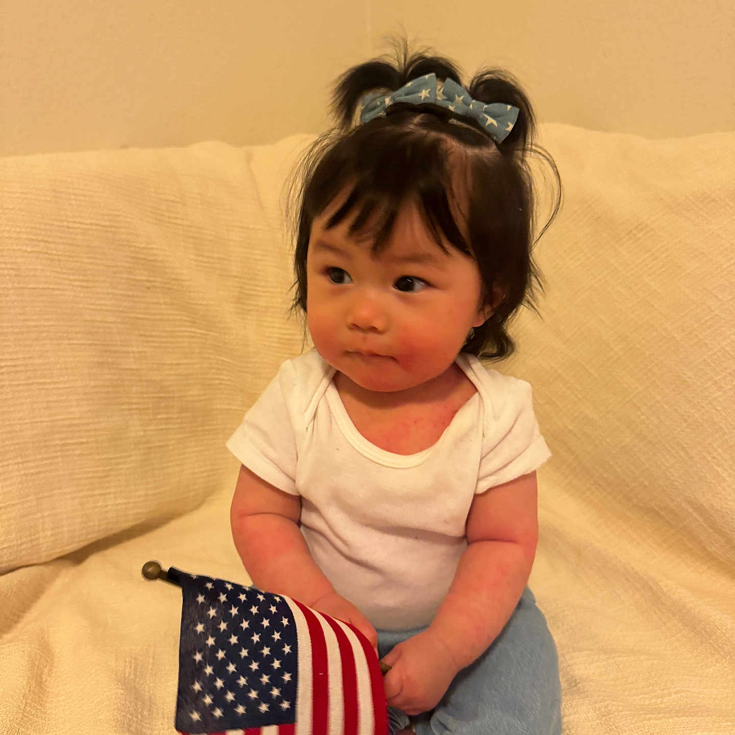 Annaya is registered to the contest to win money with this photo: toddler, child, baby, flag, american_flag, bow, hair_accessory, white_shirt, blue_pants, sitting, couch, indoor, curious, portrait, person, infant, cute, soft_lighting, young_child, casual_clothing