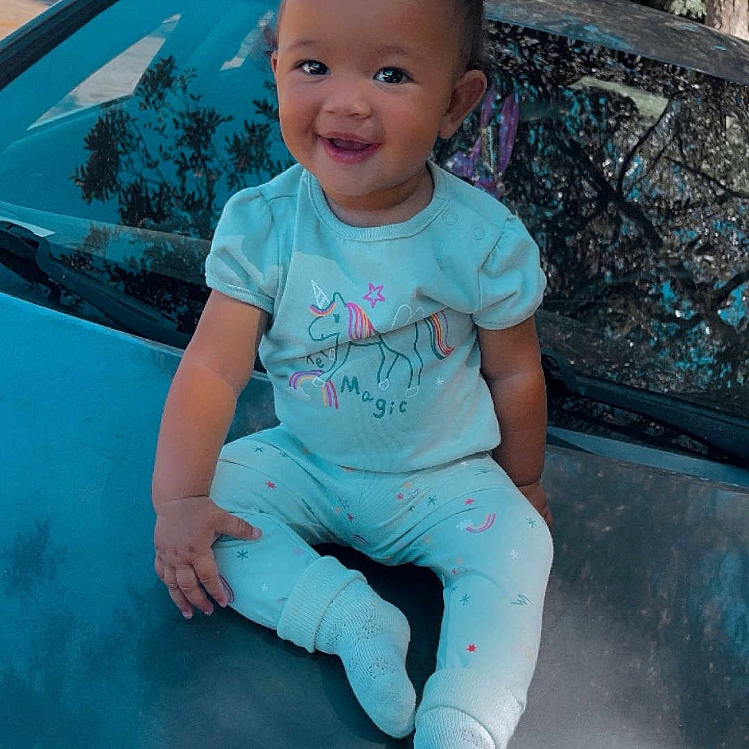Zariyah joined the competition — help win amazing prizes! baby, car, clothing, face, happy, head, hosiery, jeans, outdoors, pants, person, photography, plant, portrait, sitting, smile, sock, transportation, tree, vehicle