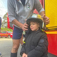 Laïhyon a rejoint le concours — aidez-le/la à gagner de superbes lots ! adult, bokeh_background, child, coat, curly_hair, family_moment, fire_truck, hand, helmet, helping_hand, hoodie, jacket, outdoor, parked_car, pavement, portrait, protective_gear, red_vehicle, smile, vehicle_door