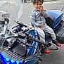 Laïhyon a rejoint le concours — aidez-le/la à gagner de superbes lots ! background, blue, casual_clothing, child, curly_hair, daylight, grey_hoodie, hand_gesture, happy, motorcycle, outdoor, people, playful, red_shoes, road, sidewalk, smile, street, urban, vehicle
