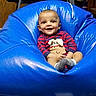 baby, child, bean_bag, blue, smiling, happy, indoor, clothing, striped_shirt, cute, person, face, socks, seated, furniture, wooden_door, floor, playful, cozy, comfort