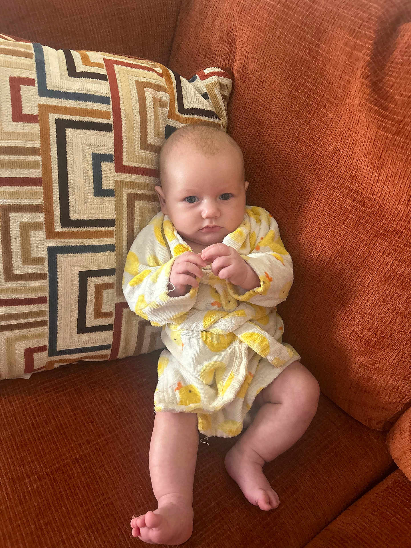 Michael joined the competition — help win amazing prizes! baby, infant, robe, duck_pattern, couch, pillow, orange_couch, sitting, barefoot, toes, looking_at_camera, portrait, home_interior, fabric, upholstery, cute, hands, legs, head, eyes