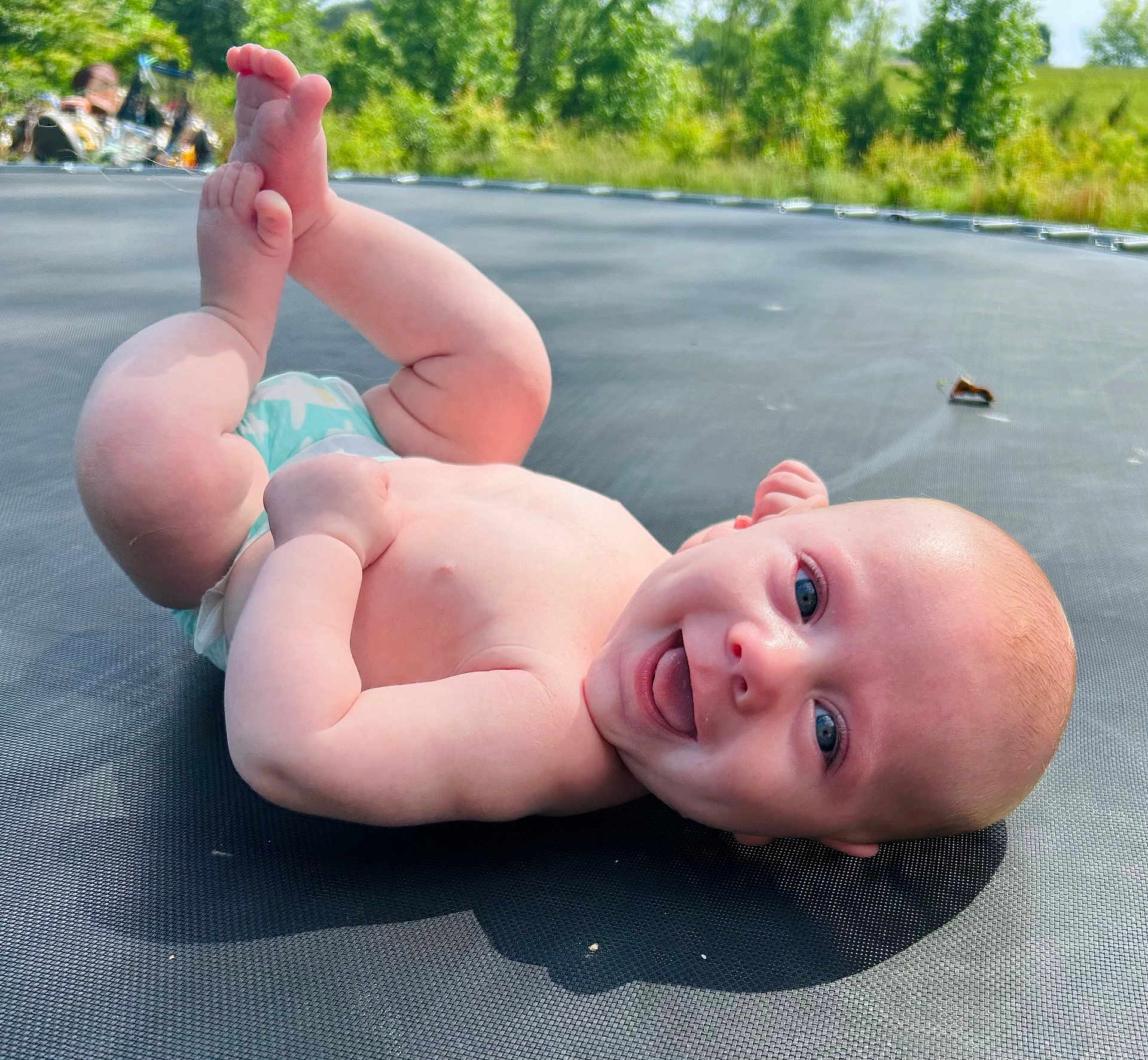 Waylon joined the competition — help win amazing prizes! baby, infant, smiling, blue_eyes, bare_chest, diaper, trampoline, outdoor, greenery, grass, sunlight, playful, happy, skin, child, nature, summer, cute, lying_down, feet_up