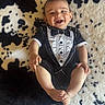 Bo is registered to the contest to win money with this photo: baby, black_and_white, blanket, child, clothing, cute, face, foot, hand, happy, indoors, infant, onesie, patterned_blanket, portrait, sitting, smile, soft_texture, tuxedo, young_child