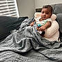 Zharron joined the competition — help win amazing prizes! baby, infant, blanket, cushion, toy, couch, window, blinds, indoor, person, child, support_pillow, white_clothing, gray_blanket, soft_texture, natural_light, face, expression, seated, home