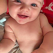Joseph is registered to the contest to win money with this photo: baby, smiling, blue_eyes, chubby, hand, blanket, red_background, hummingbird, cute, infant, skin, portrait, person, happy, lying_down, closeup, face, baby_skin, child, indoors