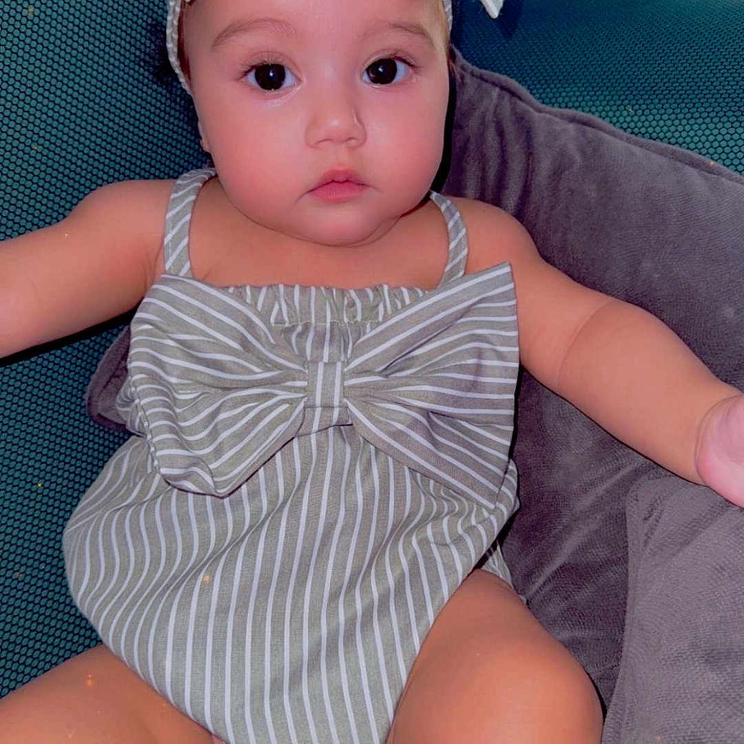 Lycia participe au concours pour gagner de l'argent avec cette photo : arm, baby, bow, chair, child, cushion, cute, eyes, face, headband, indoors, infant, legs, person, plump, relaxed, romper, seated, skin, striped_clothing