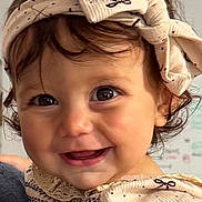 Melanie is registered to the contest to win money with this photo: baby, child, smile, headband, bow, dress, hand, face, eyes, cute, happy, portrait, infant, clothing, person, skin, hair, indoor, closeup, young