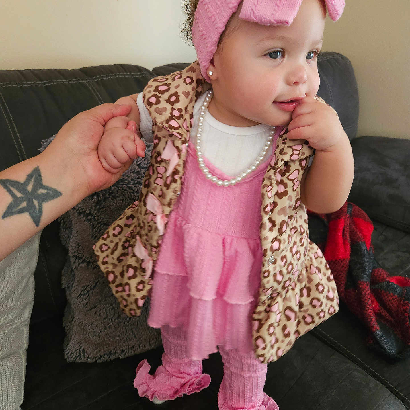 Coraleez is registered to the contest to win money with this photo: toddler, child, pink_clothing, headband, bow, pearl_necklace, leopard_print, vest, couch, hand_holding, adult_hand, living_room, blanket, curly_hair, pink_pants, ruffled_pants, cute, portrait, indoor, person
