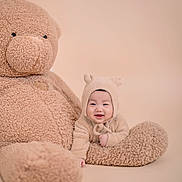Ian joined the competition — help win amazing prizes! baby, teddy_bear, plush_toy, smiling, cute, fuzzy, beige, soft_texture, child, portrait, indoors, cozy, hat, happy, toy, sitting, infant, warm, cuddly, studio