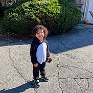 Yazan joined the competition — help win amazing prizes! child, smiling, curly_hair, onesie, black_and_white, sneakers, pavement, cracks, bush, greenery, pumpkin, building, window, sunlight, shadow, outdoor, fall, happy, person, toy