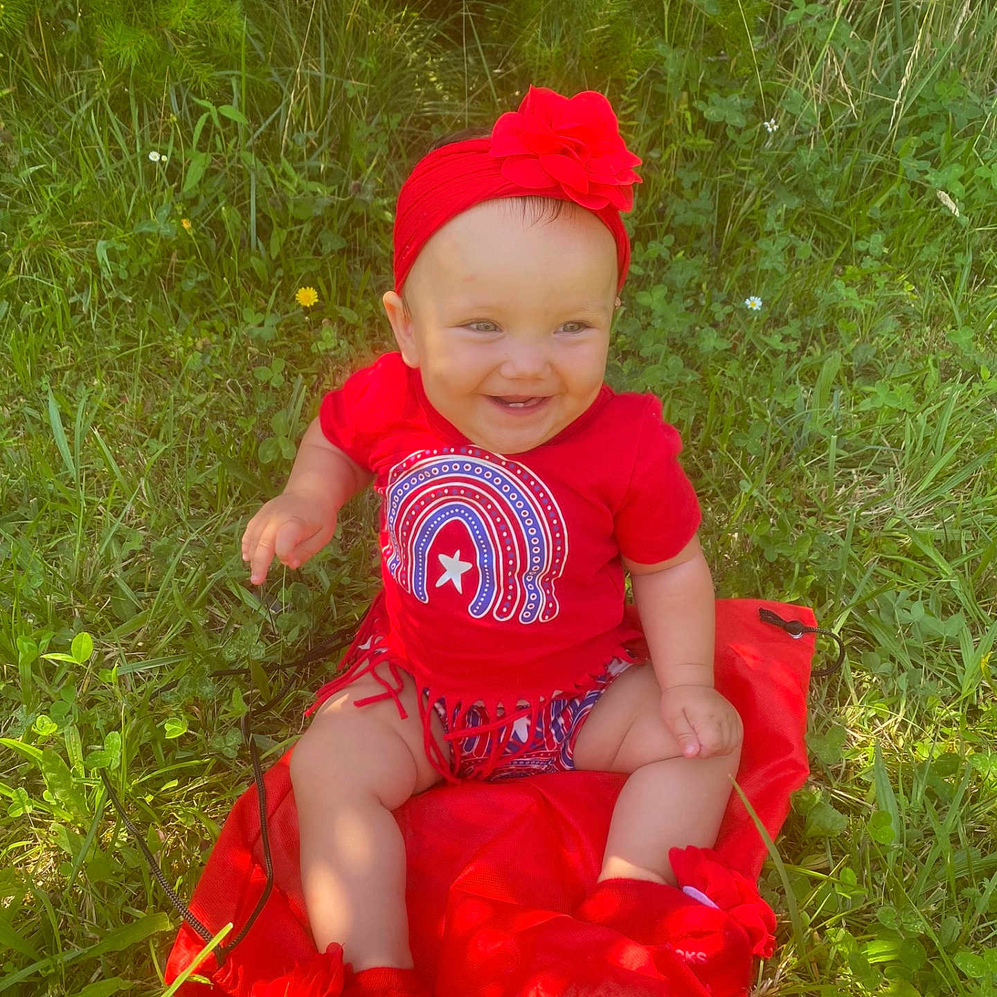 Annsley joined the competition — help win amazing prizes! baby, blanket, child, cute, flower, footwear, grass, greenery, happy, headband, headwear, infant, nature, outdoor, person, red_clothing, sitting, smiling, summer, sunlight