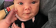 Annsley is registered to the contest to win money with this photo: baby, infant, face, hand, blanket, clothing, onesie, purple, black, person, human, cute, expression, chubby_cheeks, indoor, portrait, young_child, holding, motion_blur, casual