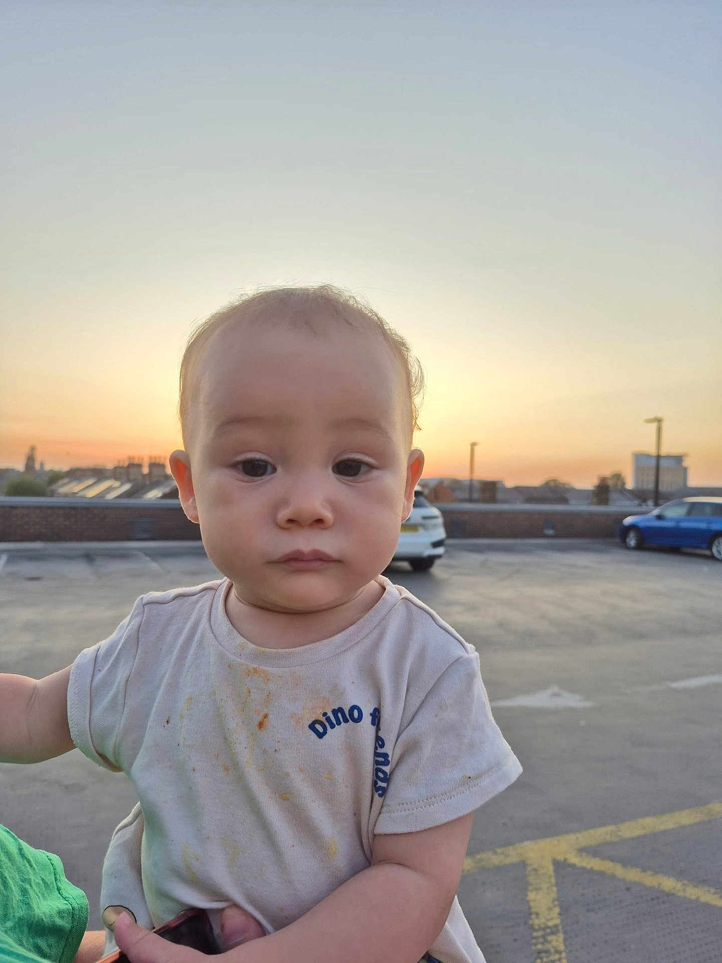 Juan joined the competition — help win amazing prizes! toddler, child, baby, outdoor, sunset, parking_lot, car, shirt, messy, person, face, expressionless, holding, urban, sky, building, blurred_background, short_sleeve, casual, daylight