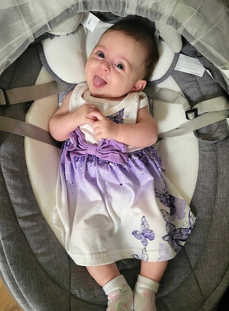 Lina a rejoint le concours — aidez-le/la à gagner de superbes lots ! baby, child, infant, dress, purple, butterfly, socks, smiling, tongue_out, seat, cushion, gray, clothing, cute, happy, person, indoors, baby_seat, playful, portrait