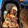 Marley is registered to the contest to win money with this photo: baby, smiling, stroller, hat, blanket, plush_toy, giraffe, elephant_toy, pacifier, indoor, flooring, wooden_floor, chair, table, child, happy, clothing, person, cozy, seat