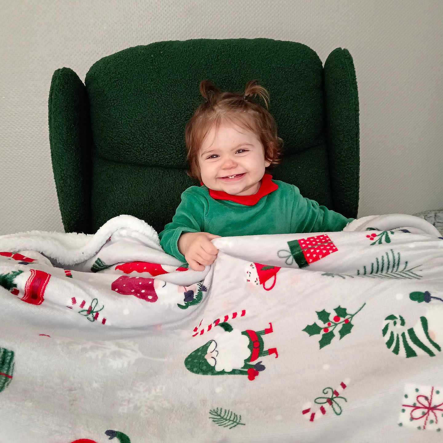 Nina a rejoint le concours — aidez-le/la à gagner de superbes lots ! blanket, chair, child, christmas, cozy, cute, face, festive, green_clothing, hair, happy, holiday, home, indoor, pattern, person, sitting, smiling, toddler, wallpaper