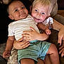 baby, toddler, child, smile, couch, blanket, person, arm, hand, clothing, shorts, white_shirt, blue_eyes, blond_hair, dark_hair, indoor, family, happy, closeup, skin