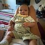 baby, infant, person, child, clothing, socks, legs, face, bedroom, television, furniture, anchor, car_seat, blanket, pajamas, indoor, relaxing, home, cute, smiling