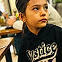 child, girl, portrait, hoodie, black_clothing, indoor, table, blurred_background, face, looking_away, casual, young, person, expression, earrings, brown_hair, sitting, restaurant, wooden_table, soft_lighting