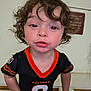 toddler, child, curly_hair, indoor, black_jersey, orange_trim, sports_jersey, bengals, facial_expression, person, young_child, portrait, cute, looking_at_camera, short_sleeves, standing, skin, hair, face, close_up