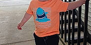 Colsyn is registered to the contest to win money with this photo: toddler, child, smiling, orange_tshirt, shark_graphic, shorts, sneakers, black_shoes, standing, railing, porch, outdoor, concrete_floor, happy, casual_clothing, person, young_child, short_hair, daylight, holding