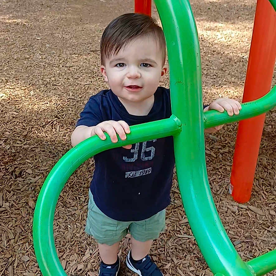 Colsyn joined the competition — help win amazing prizes! casual_clothing, child, curious, daylight, fun, green_bars, outdoor, park, person, play, play_equipment, playground, short_hair, shorts, smiling, sneakers, standing, toddler, wood_chips, young_child