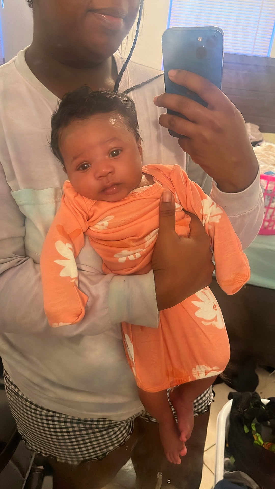 Janivea joined the competition — help win amazing prizes! baby, person, mirror, selfie, orange_clothing, flower_pattern, indoor, bedroom, window, curly_hair, holding, smile, phone, reflection, plaid_shorts, skin, hand, foot, fabric, casual