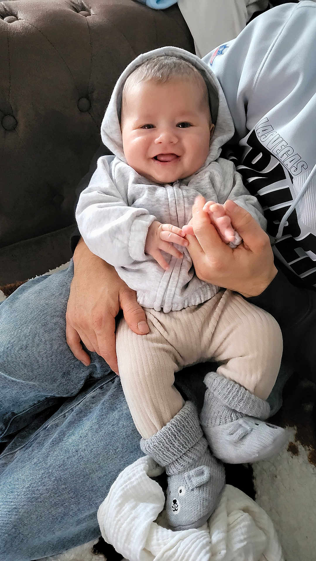 Amenadiel a rejoint le concours — aidez-le/la à gagner de superbes lots ! baby, smiling, hoodie, socks, adult_hand, couch, jeans, person, indoor, cute, knitted_socks, happy, child, cozy, infant, holding_hands, soft_clothing, toddler, footwear, blanket