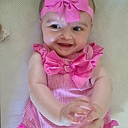 Màya is registered to the contest to win money with this photo: adorable, baby, cheerful, child, clapping, closeup, cute, face, hands, happy, headband, infant, lying_down, pink_bow, pink_dress, playful, portrait, ribbons, smiling, white_background