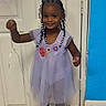 child, girl, toddler, portrait, smiling, standing, dress, lavender_dress, hair_bows, braids, beads, sandals, balloon, balloon_ribbon, birthday, indoors, door, tile_floor, blue_wall, cartoon_decor