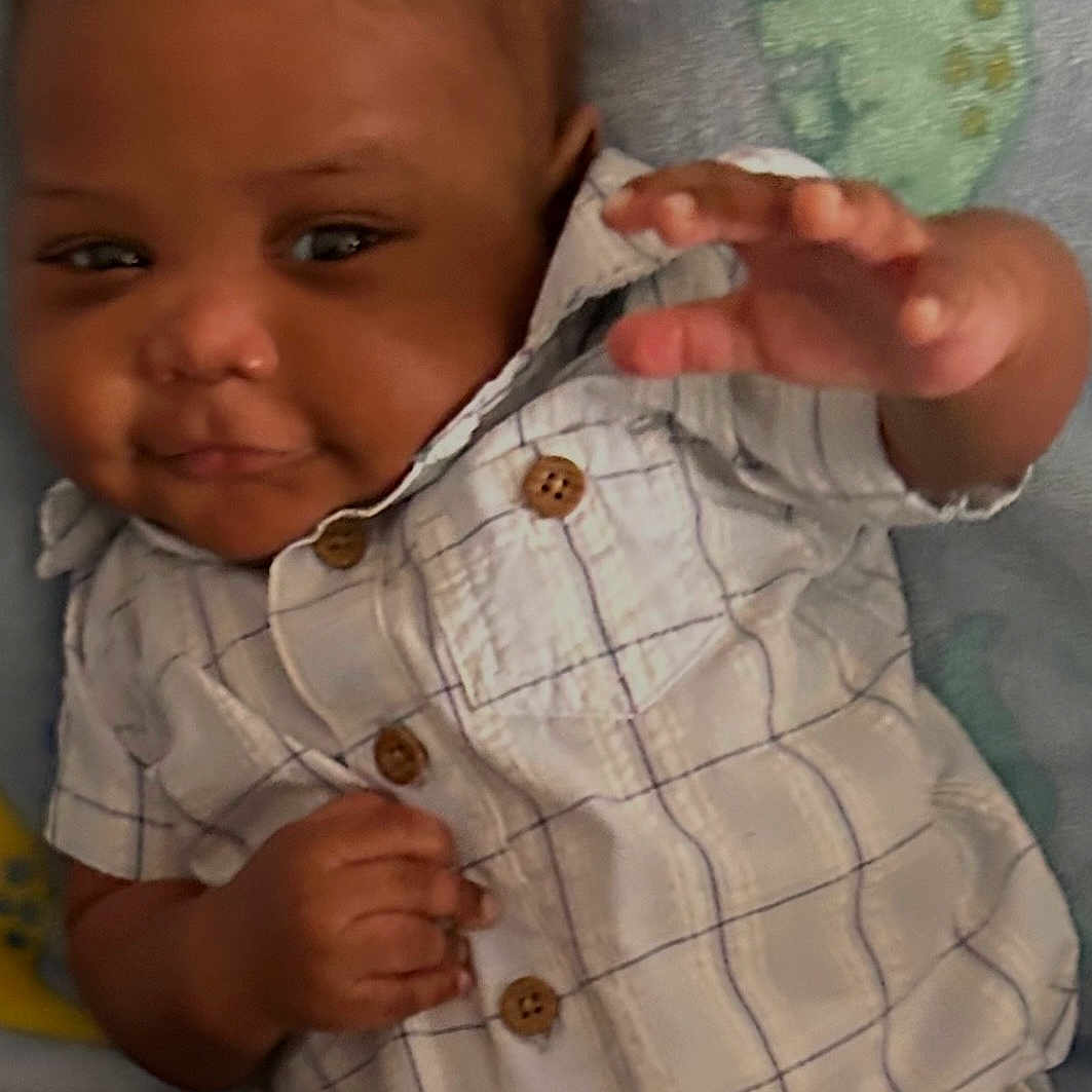 Zeke joined the competition — help win amazing prizes! baby, infant, child, shirt, clothing, button, hand, face, lying_down, blanket, soft, cute, smiling, portrait, indoor, skin, young_child, expression, reaching, baby_boy