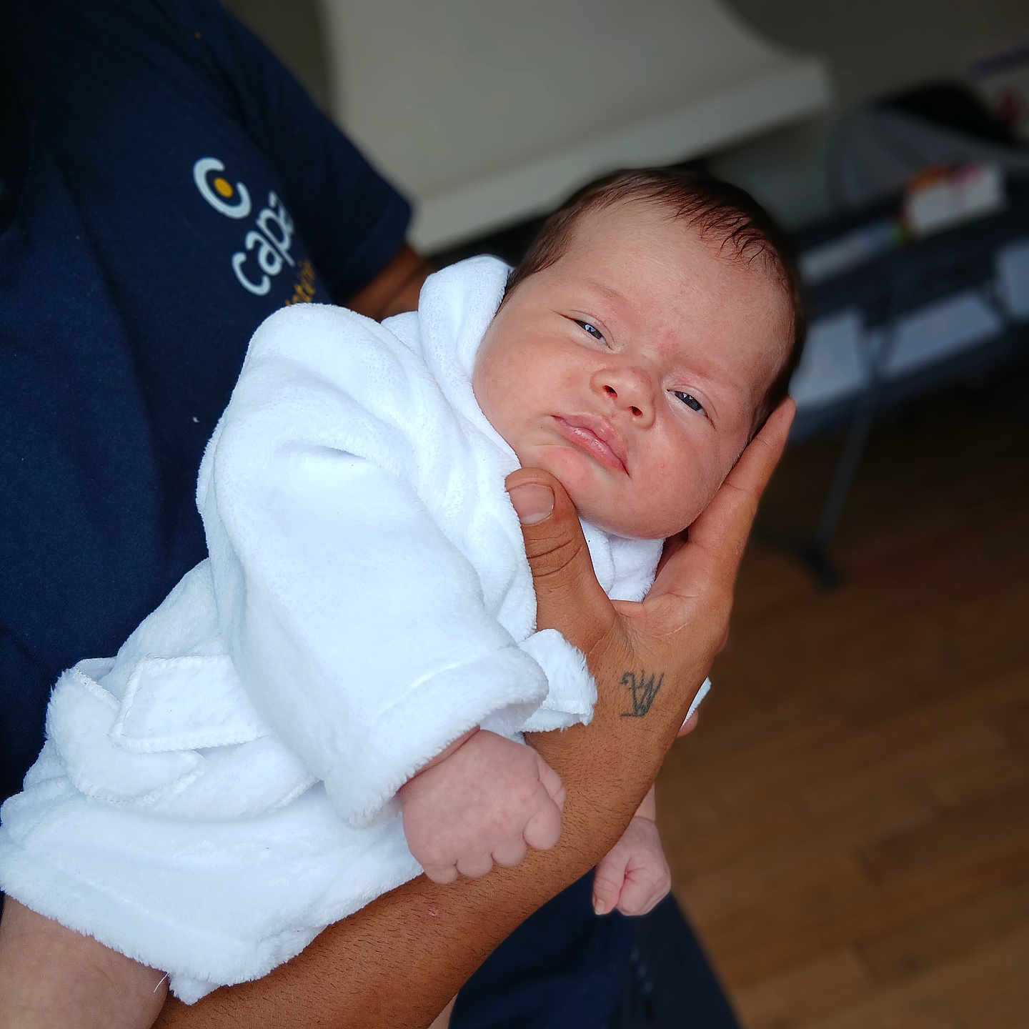 Marta a rejoint le concours — aidez-le/la à gagner de superbes lots ! baby, blurred_background, close_up, clothing, cute, expression, face, hand, holding, human, indoor, infant, newborn, person, portrait, skin, sleepy, tattoo, white_robe, wooden_floor