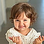 baby, background_blur, casual_clothing, child, curly_hair, cute, expression, eyes, face, floral_pattern, hands, happy, indoor, person, portrait, skin, smiling, toddler, white_top, young_child
