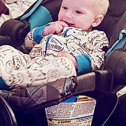 Rodger joined the competition — help win amazing prizes! baby, child, car_seat, pajamas, dinosaur_print, indoor, bed, pillow, blanket, smiling, happy, cute, infant, person, face, clothing, furniture, relaxing, young_child, comfort