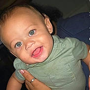 Ezekiel is registered to the contest to win money with this photo: baby, child, infant, portrait, smiling, happy, face, eyes, open_mouth, short_hair, green_outfit, onesie, held, adult_hand, indoor, flash_photography, close_up, seated, family, candid
