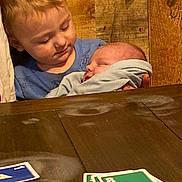 Gunnison joined the competition — help win amazing prizes! child, baby, sleeping, holding, wooden_wall, table, cards, playing_cards, blue_shirt, blanket, tender_moment, indoor, two_children, family, love, peaceful, portrait, young_child, infant, casual