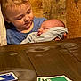 child, baby, sleeping, holding, wooden_wall, table, cards, playing_cards, blue_shirt, blanket, tender_moment, indoor, two_children, family, love, peaceful, portrait, young_child, infant, casual