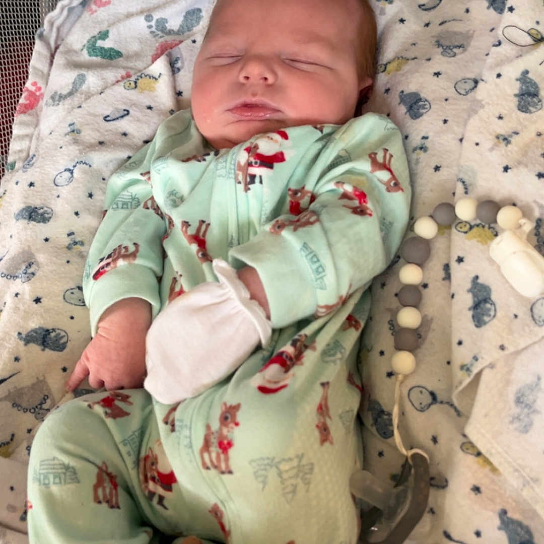 Gunnison is registered to the contest to win money with this photo: baby, baby_clothing, blanket, child, cozy, crib, cute, footprint_pattern, indoors, infant, mittens, newborn, onesie, pacifier, peaceful, reindeer, resting, sleeping, soft_toy, toy