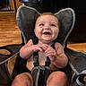 Gunnison is registered to the contest to win money with this photo: baby, child, infant, smiling, happy, portrait, sitting, high_chair, harness, indoor, home, wood_floor, furniture, baby_seat, hands, blue_eyes, blond_hair, bare_arms, photography, family