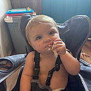 Gunnison is registered to the contest to win money with this photo: baby, child, infant, high_chair, eating, snack, food, smiling, portrait, indoor, home, kitchen, toy, colorful, blond_hair, blue_eyes, seated, harness, messy_eating, close_up