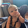 baby, child, infant, high_chair, eating, snack, food, smiling, portrait, indoor, home, kitchen, toy, colorful, blond_hair, blue_eyes, seated, harness, messy_eating, close_up