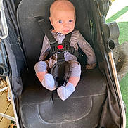 Gunnison is registered to the contest to win money with this photo: baby, baby_clothes, black, blue_eyes, casual_clothing, child, fabric, footwear, grass, infant, leaves, onesie, outdoor, person, pout, seat, straps, stroller, sunlight, white_socks