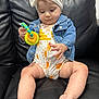baby, child, denim_jacket, headband, toy, couch, leather, sitting, curious, clothing, foot, hand, face, indoor, infant, cute, white, yellow, orange, play