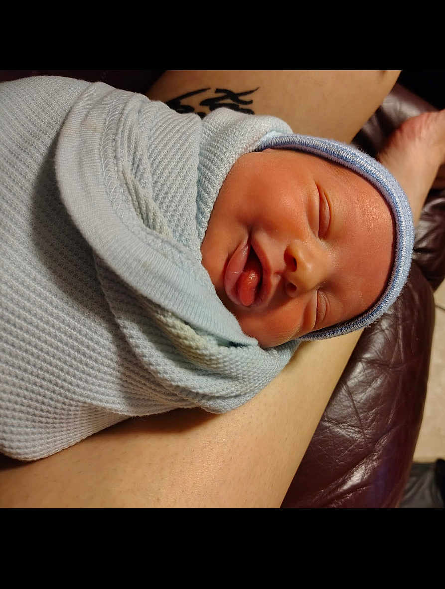 Sawyer is registered to the contest to win money with this photo: newborn, baby, sleeping, wrapped, blanket, blue, infant, face, peaceful, resting, leg, tattoo, skin, closeup, cozy, soft, indoors, person, portrait, human