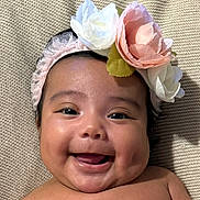 Liana is registered to the contest to win money with this photo: baby, child, smiling, face, headband, flower, cheeks, skin, portrait, closeup, happy, infant, head, cute, lying_down, texture, blanket, warm, soft, indoors